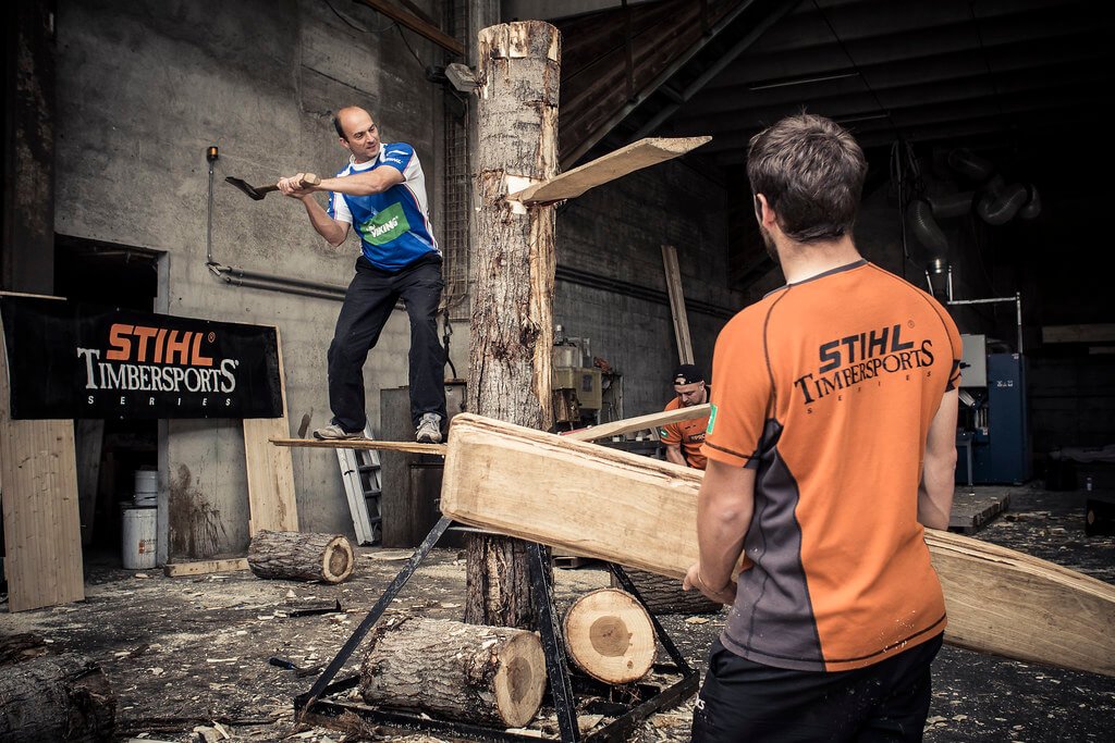 A man wielding an axe against a thick tree trunk, competing in the Stihl Timbersports series